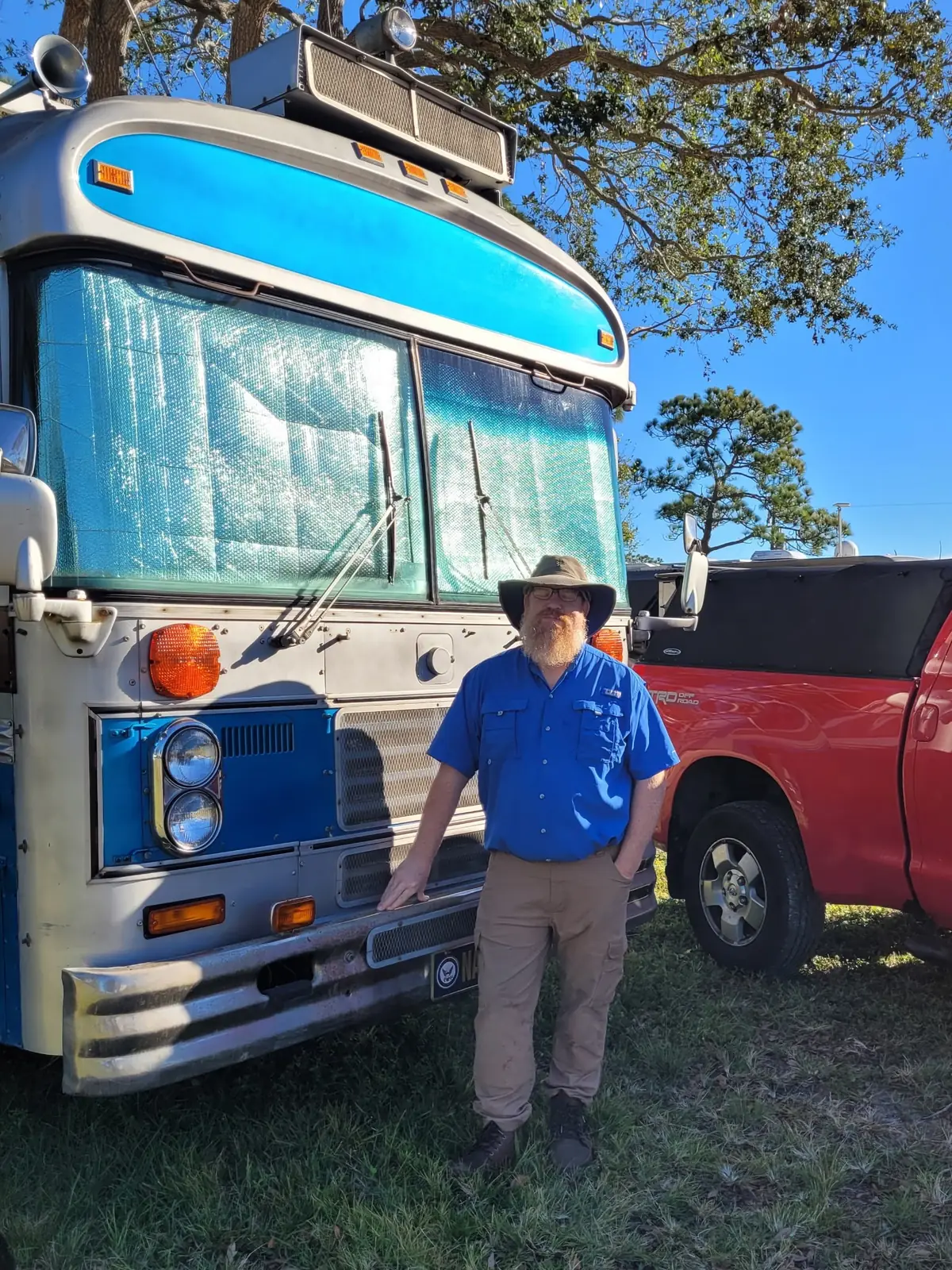 Paul standing at the front of his blue bus RV